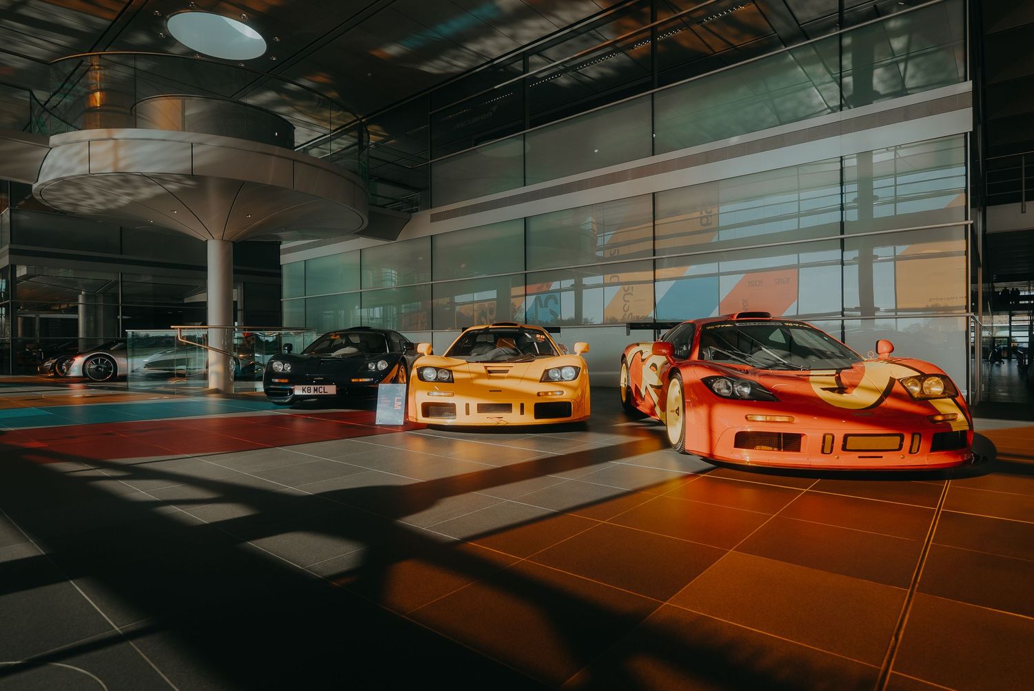 Panoramic view of luxury sports cars parked in a dimly lit underground garage with dramatic orange lighting.