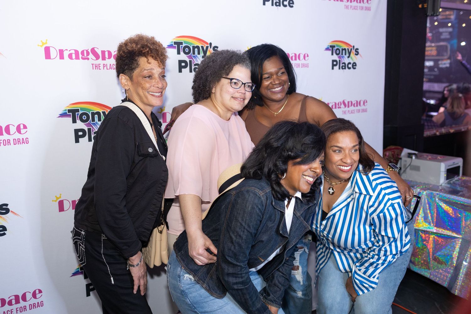 Group of people laughing and socializing at an entertainment event with pink signage in the background.