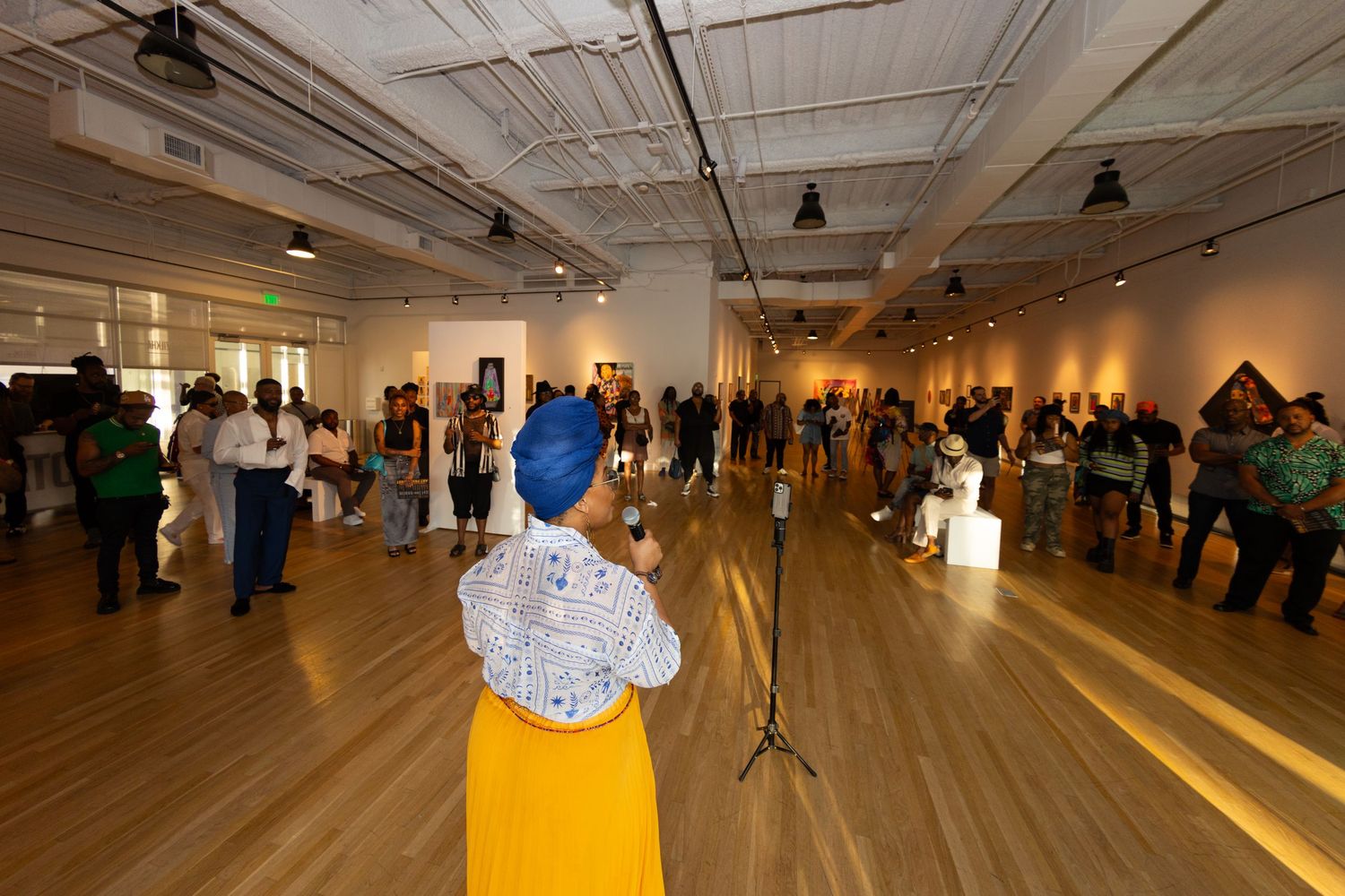 Gallery visitors walk through a bright exhibition space with white walls and wooden floors viewing artwork displays.