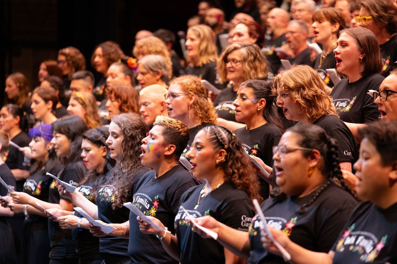 A large choir of people in black attire singing together during a performance on stage.