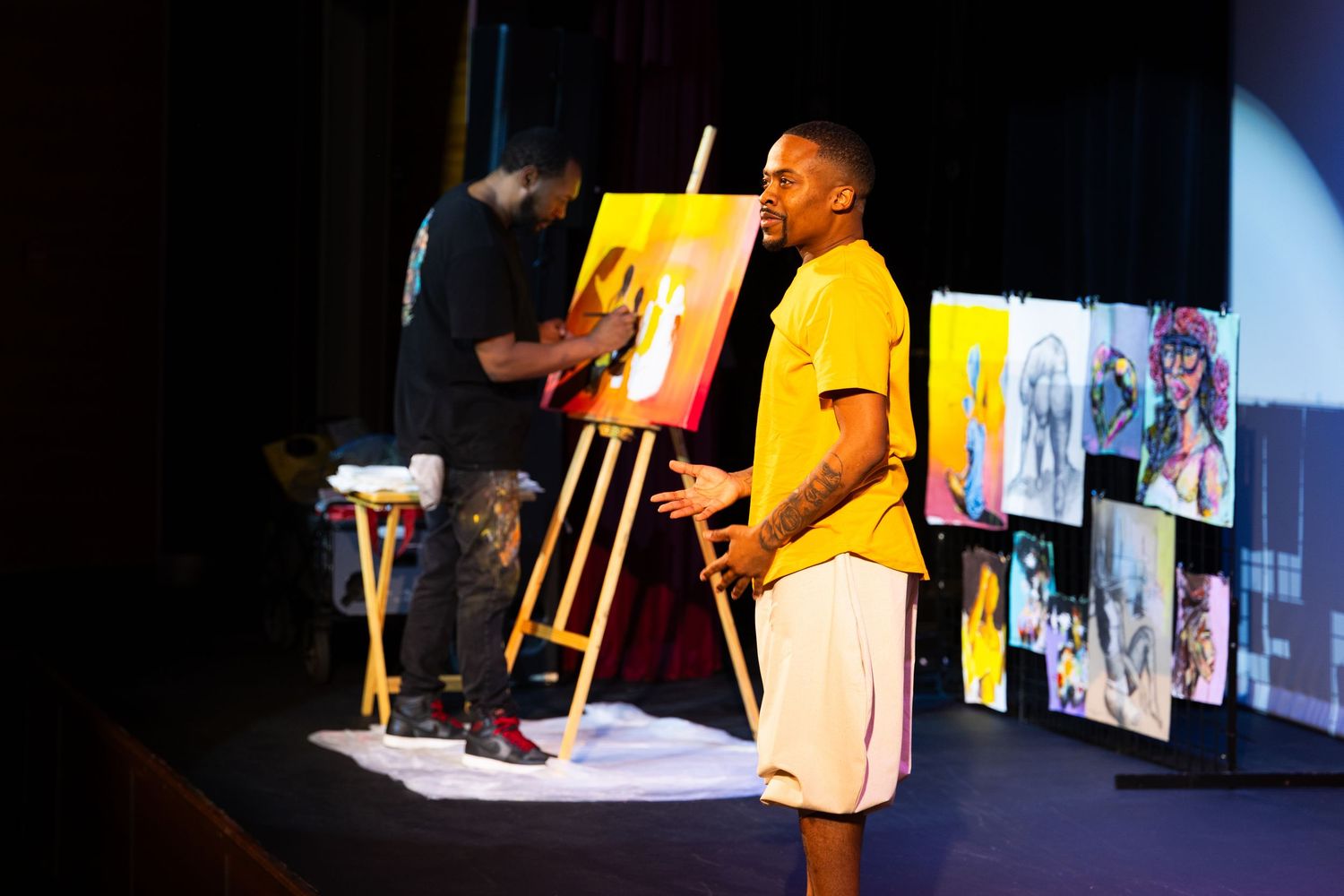 Two performers in bright yellow and white outfits engage with the audience during a stage performance.
