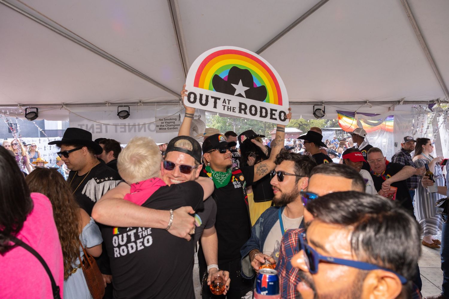 A crowded tent gathering at Out in the Rodeo event with attendees wearing sunglasses and western attire.