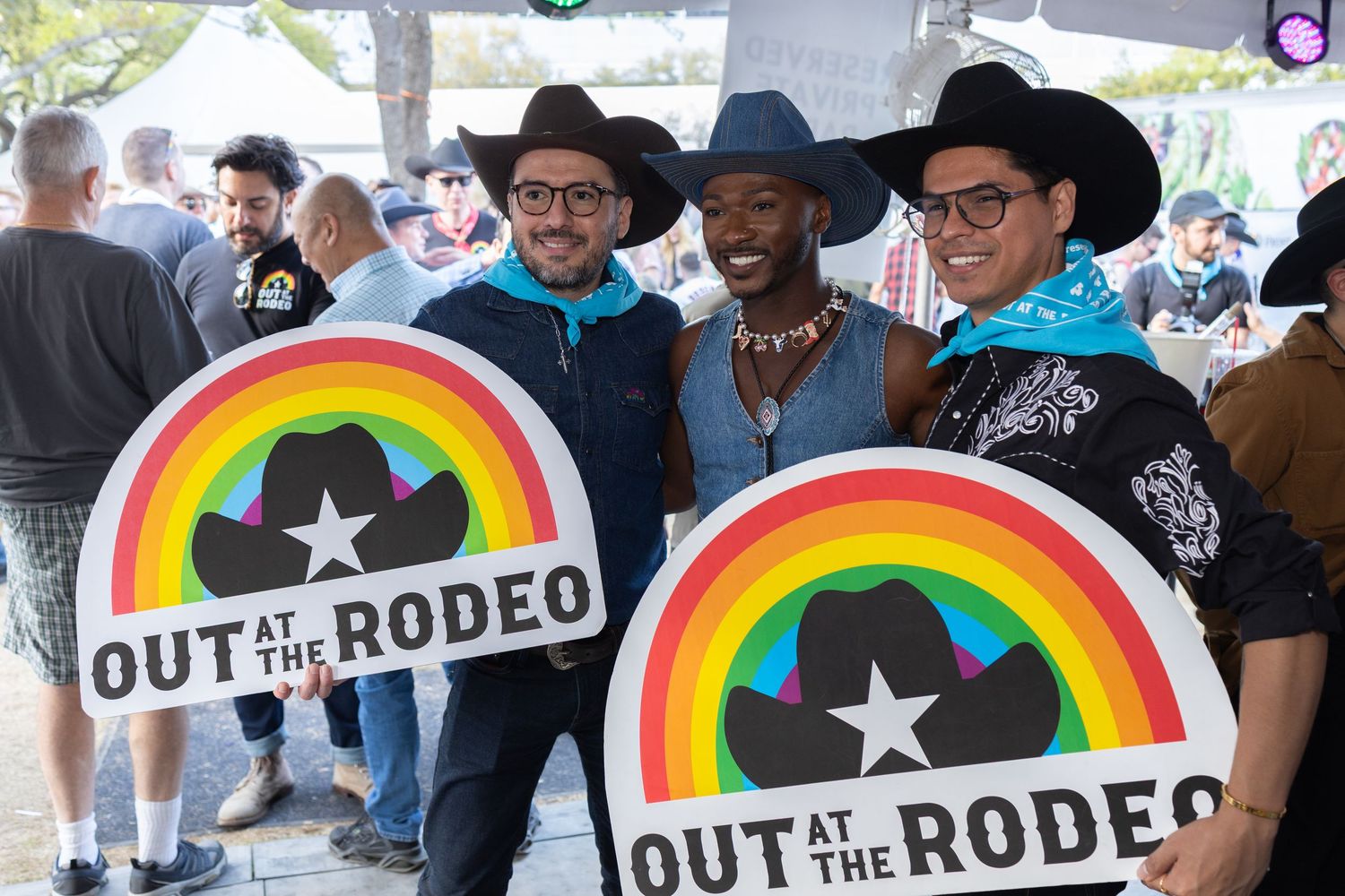 Rainbow pride flags with 'Out at the Rodeo' text displayed at a crowded LGBTQ event.
