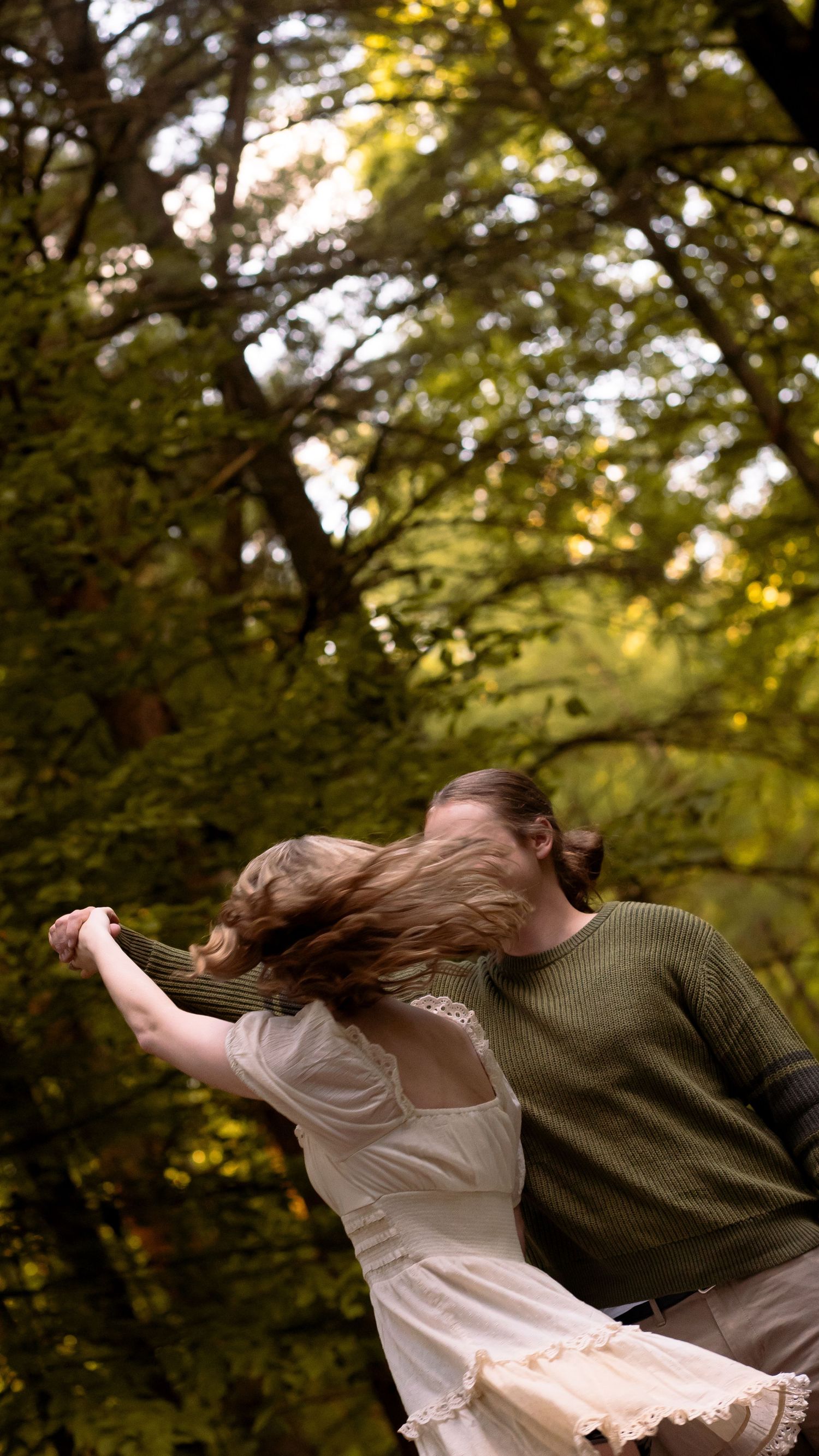 A couple dances in a forest setting during golden hour, their hair flowing with movement as they spin together.