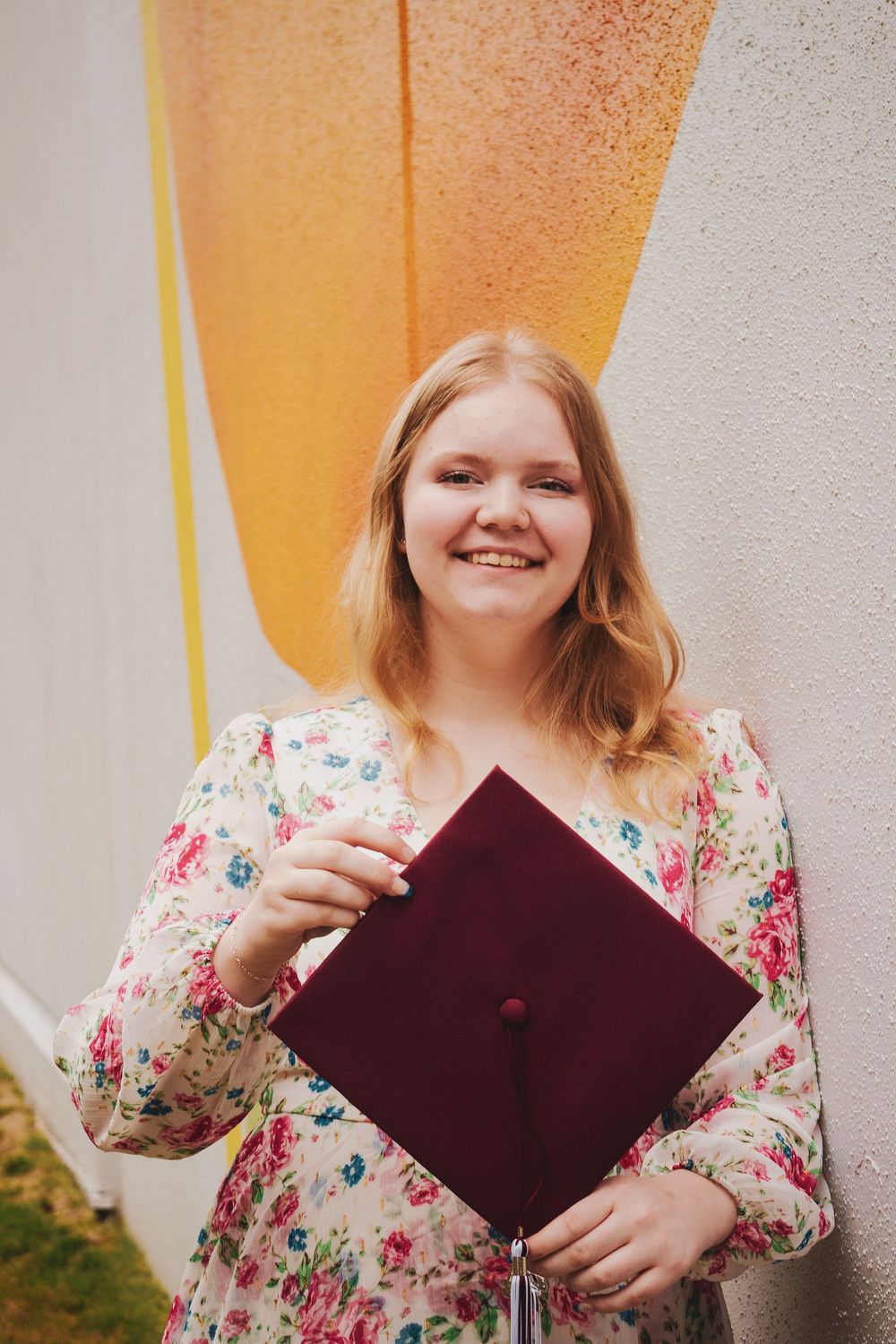 A person in a floral dress holds and examines a burgundy graduation cap in a series of progressive shots.