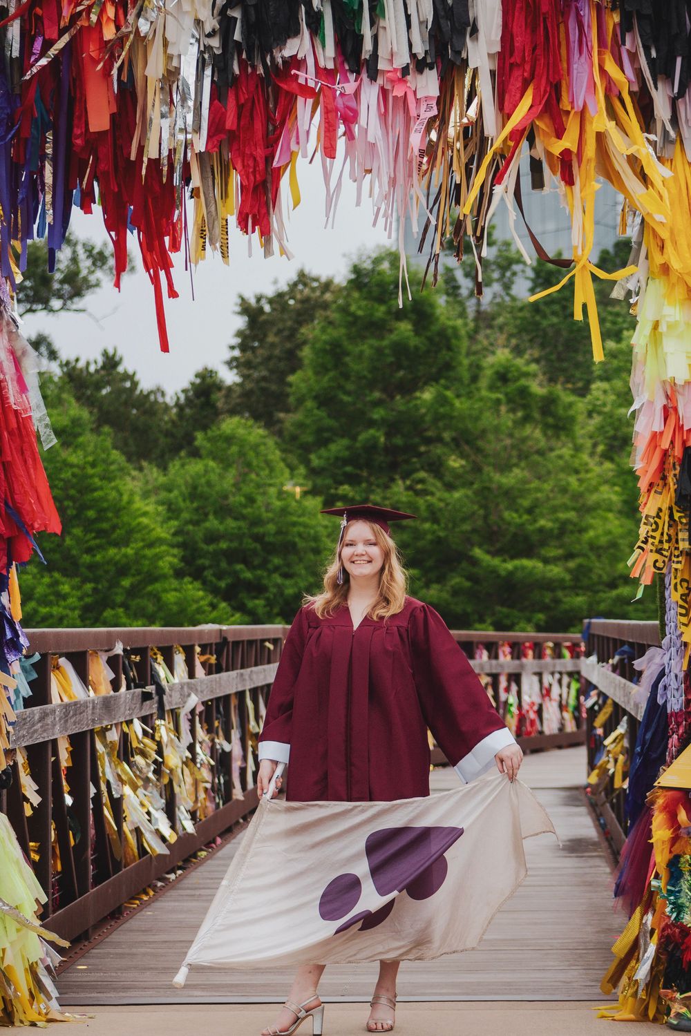 A person in a burgundy dress twirls on a wooden bridge decorated with colorful ribbons and streamers.