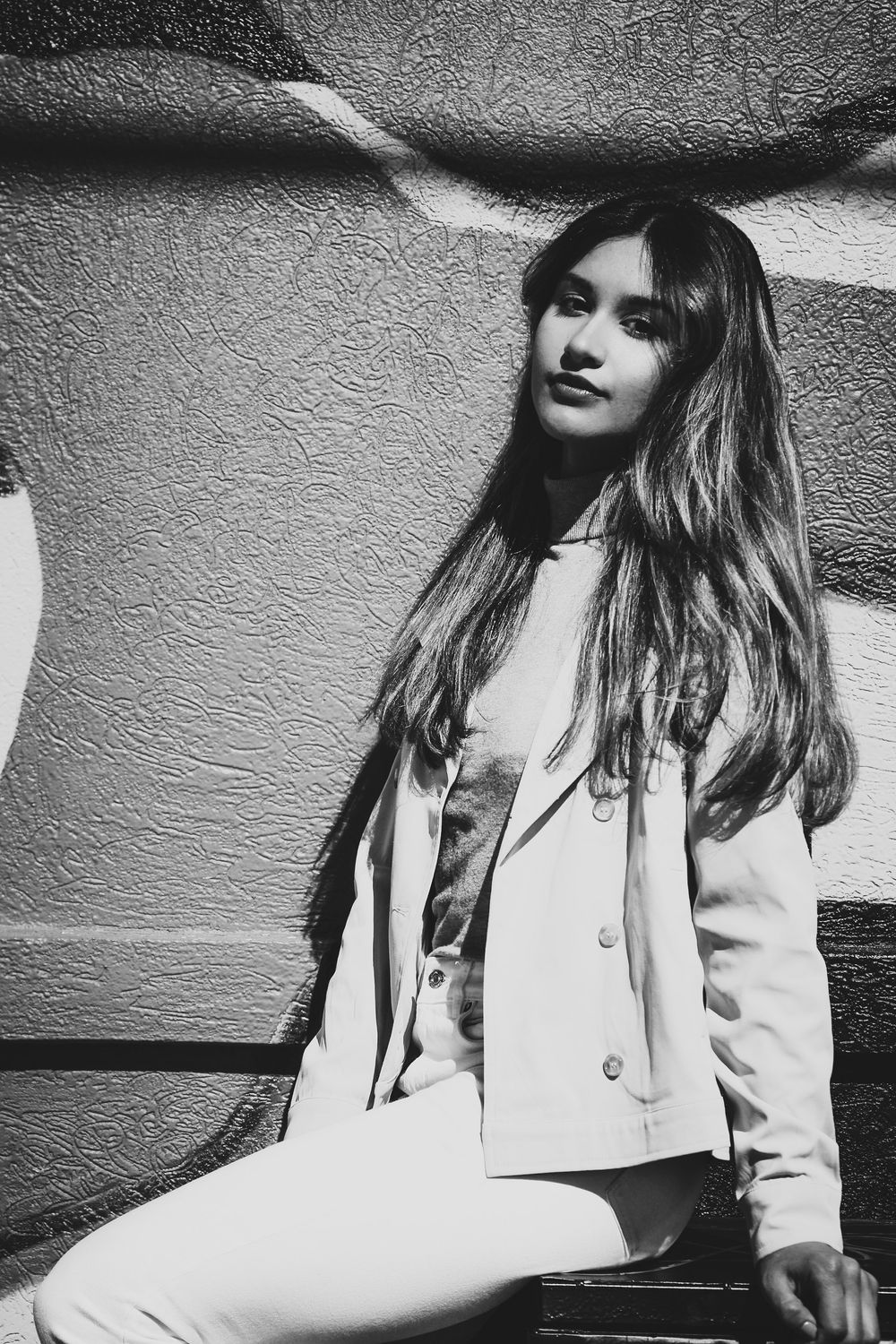 A black and white artistic portrait series showing someone in a light-colored blazer against a textured wall.