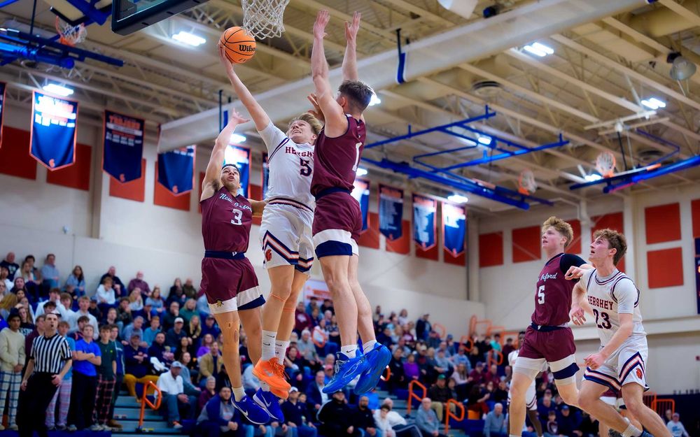 Trojans player rises above defenders for a basket with the crowd watching in the stands by SportsFox Photography, Hershey PA.