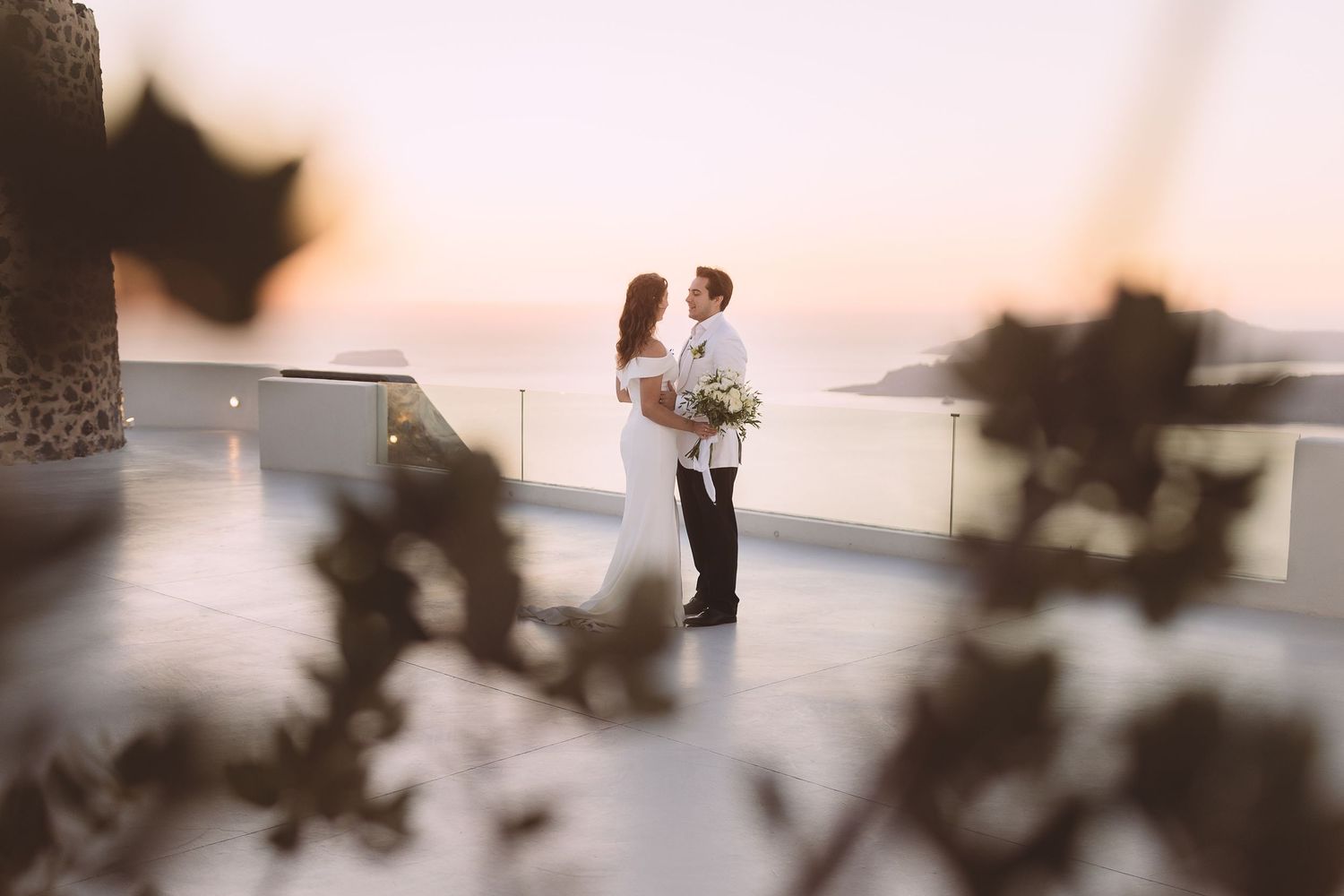 A couple stands on a balcony at El Viento, Santorini at sunset with caldera views behind them.