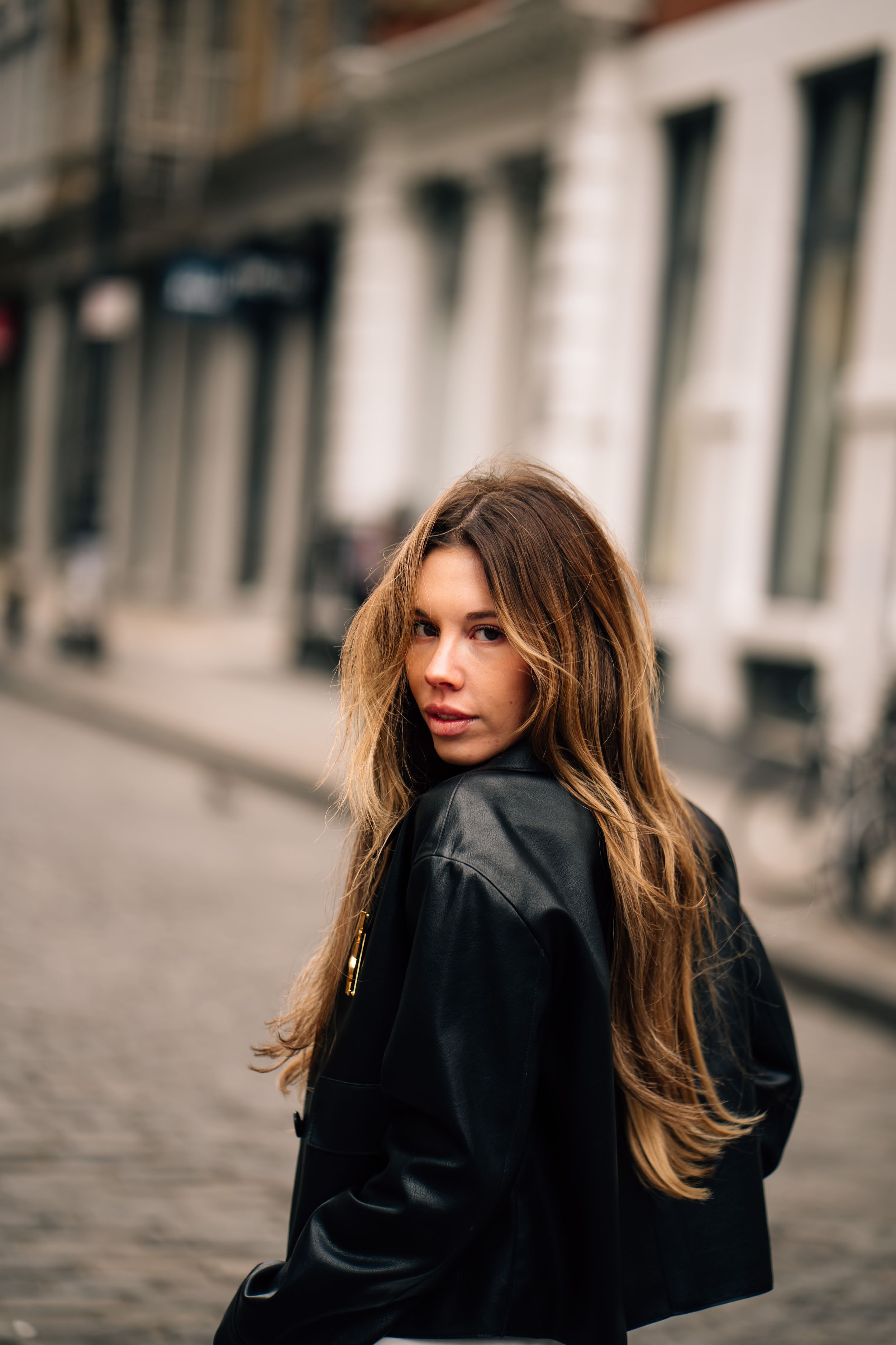 A series of five connected photos showing a person with long hair in a black jacket walking on a cobblestone street.
