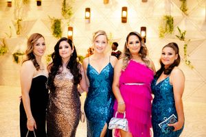 A group in formal attire poses together at an elegant event wearing sequined and colorful evening gowns.