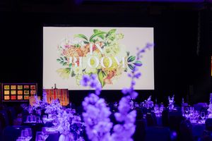 Concert stage illuminated with purple lights and floral decorations displaying a digital screen in the background.