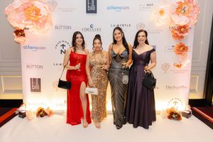 Four people in formal evening gowns pose together at a glamorous event with floral decorations.