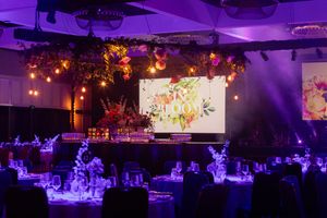 Large event space decorated with purple uplighting and hanging floral arrangements.