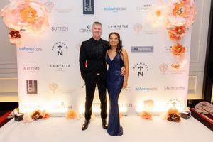 Formal event backdrop with sponsor logos and orange floral decorations against a white wall.