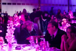 An elegant event space filled with guests under dramatic purple lighting and decor.