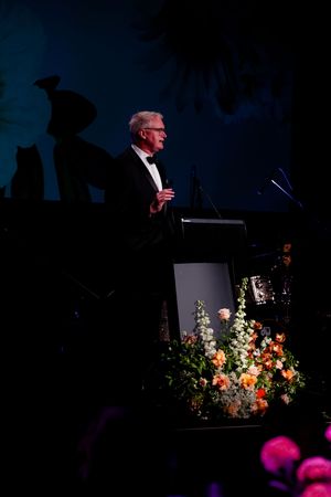 A podium decorated with colorful floral arrangements stands on a darkened stage with blue lighting.