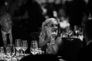 A candid black and white photo of guests enjoying a formal dinner event with wine glasses on the table.
