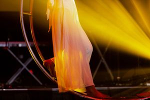 A flowing white dress silhouetted against golden stage lights on an aerial hoop performance.