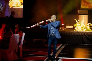 A performer sings passionately on stage with dramatic lighting and fire effects in the background.