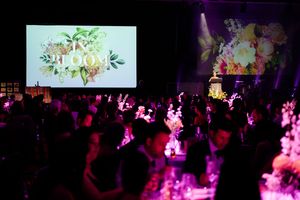Silhouettes of party attendees dancing under purple lights with projected floral designs on screens.