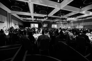 Wide panoramic view of dimly lit ballroom filled with guests at formal gathering.