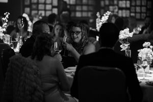 Black and white photo of guests dining at an elegant reception with floral centerpieces.
