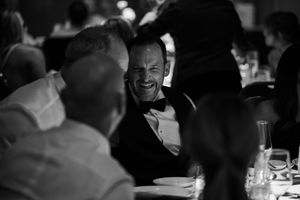 Black and white candid shot of guests sharing laughter at a formal dinner gathering.