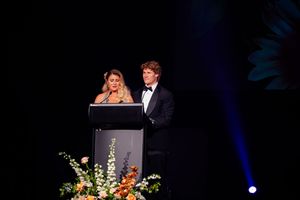 Speakers present at a podium decorated with flowers during an evening event.