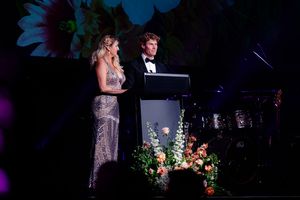 Stage performance with dramatic lighting and floral arrangements in dark blue and purple tones.