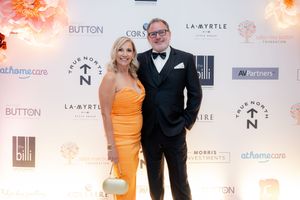 A couple poses at a formal event in front of a step-and-repeat banner wall with sponsor logos.