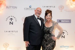 Guests at a formal gala event posing in front of a branded backdrop with corporate sponsor logos.