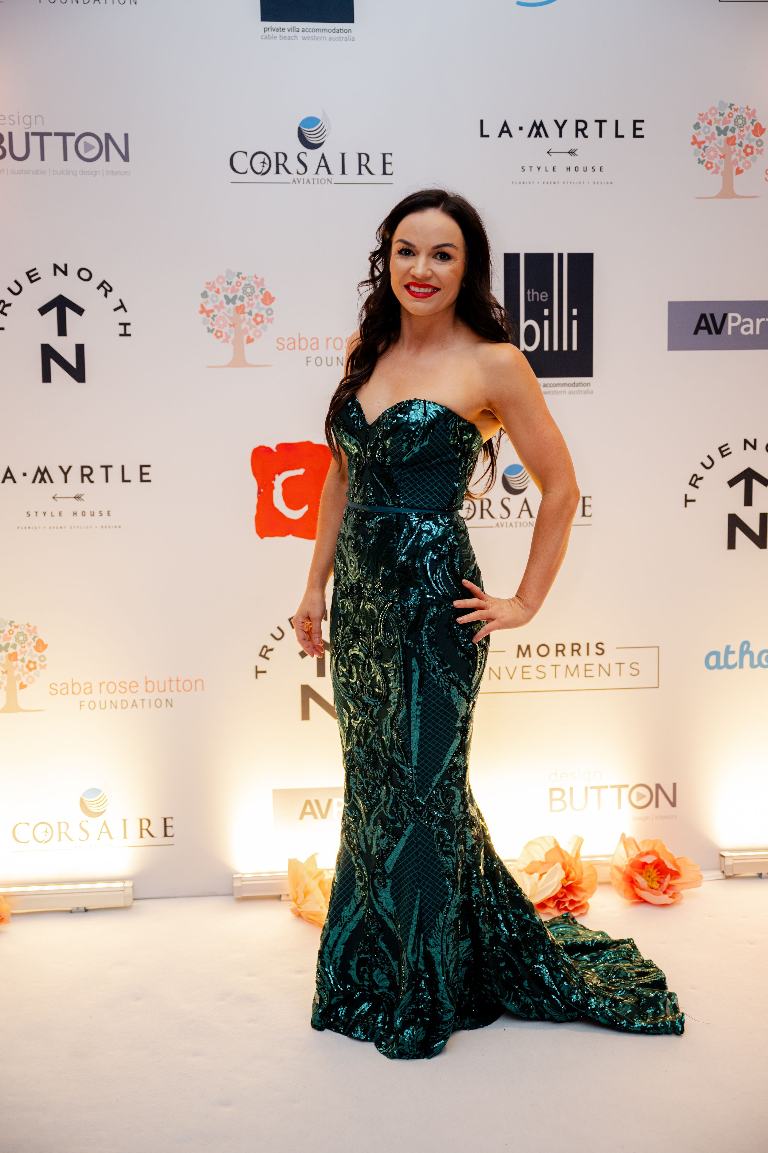 A person poses on a red carpet in a stunning emerald green velvet mermaid gown at an elegant event.