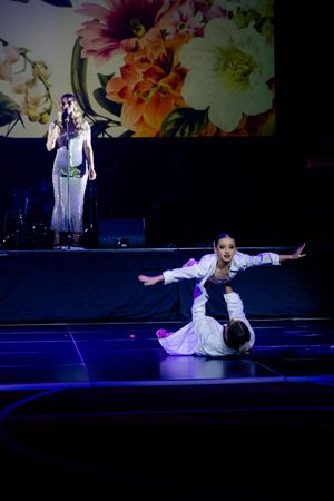 Dramatic dance performance on dark stage with floral backdrop and blue lighting effects.