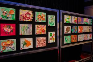 A display wall shows multiple colorful art pieces in frames against a dark background.