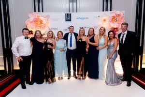 A group poses for a formal photo against a branded backdrop at an elegant event.