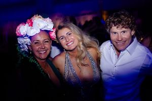 Three guests celebrate together at a festive evening party with colorful lighting.