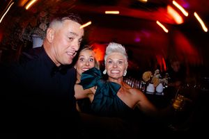Red-lit nightclub or party venue with people dancing and socializing in a dimly illuminated atmosphere.
