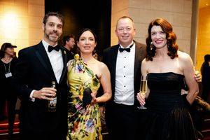 Two couples in formal attire pose with champagne glasses at an elegant event.