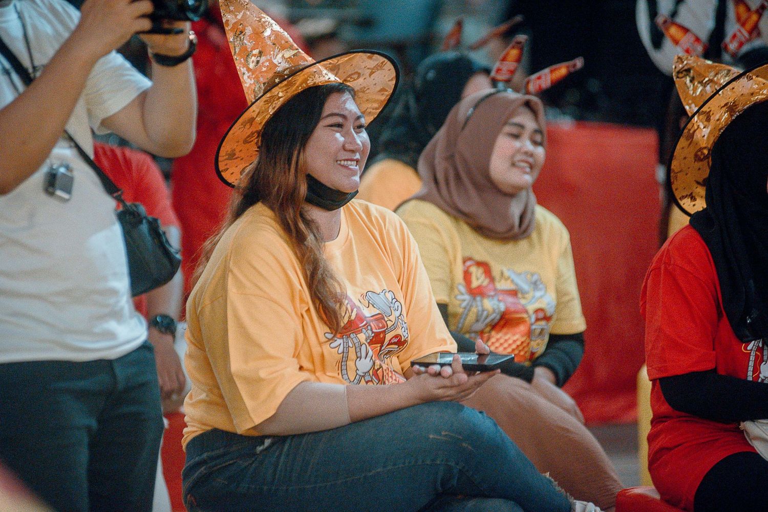Sports fans in orange and red team colors react with excitement while watching a game in stadium seats.