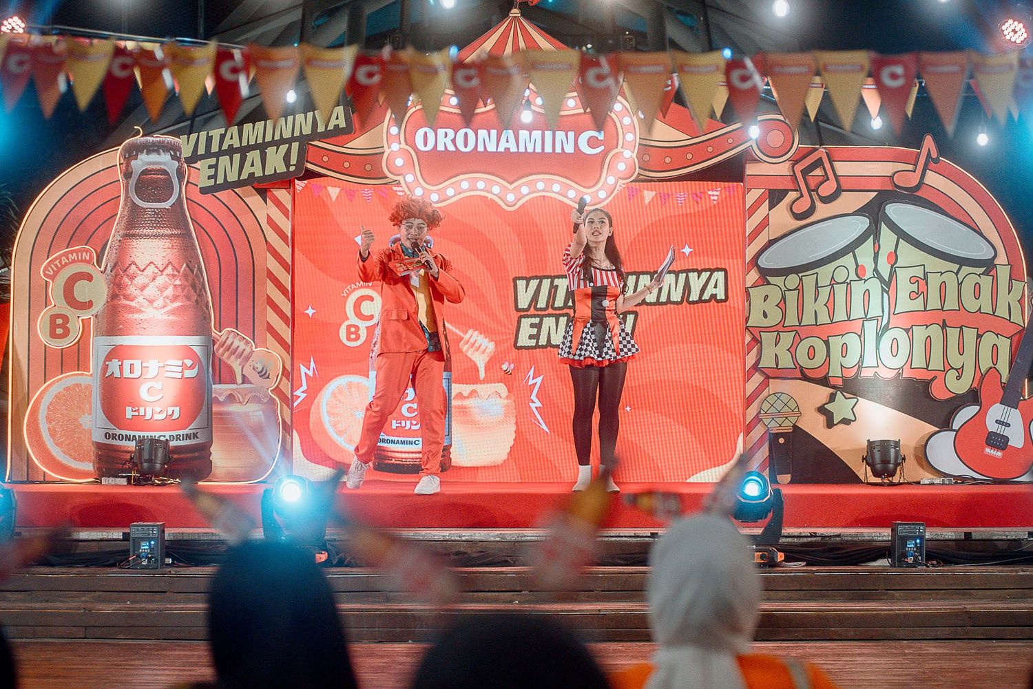A vibrant red stage backdrop with decorative banners and performers during what appears to be a promotional event.