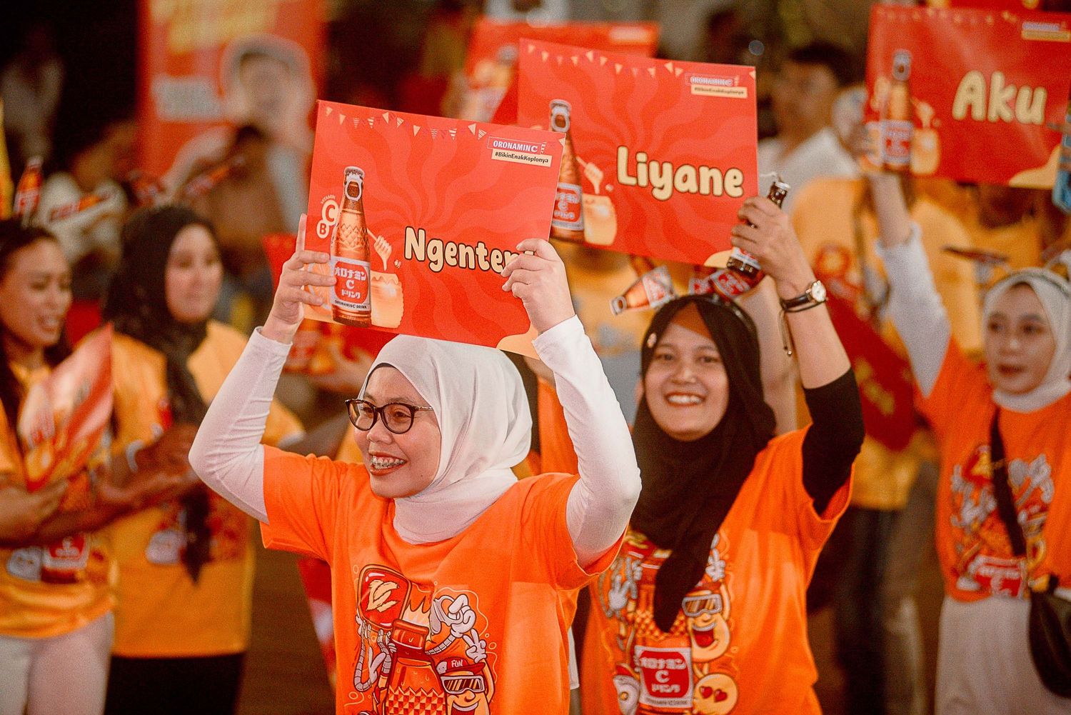 Enthusiastic participants in orange t-shirts hold up red cards during a group event celebration.