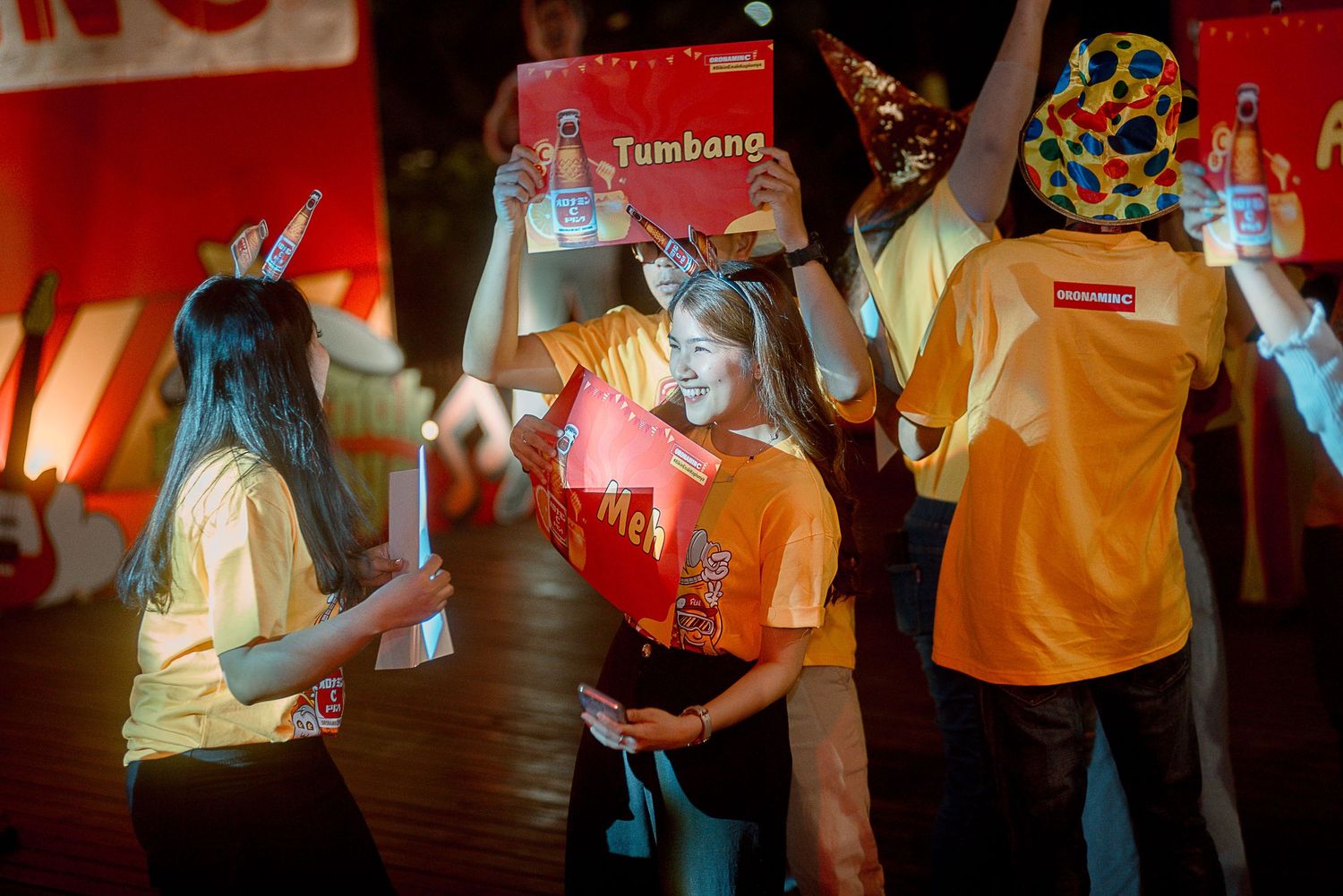 A group of people dance and socialize at a lively party with red lighting and orange decor in the background.