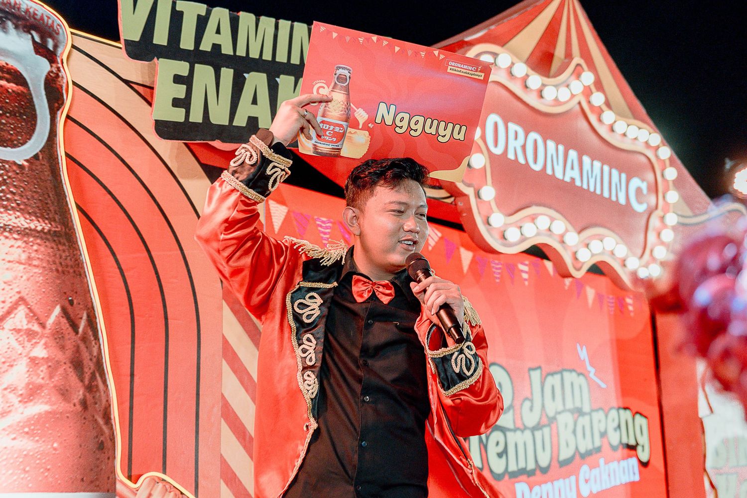 Concert stage with red lighting and large text displays showing words like 'Vitamin' and 'Ena' during a performance.