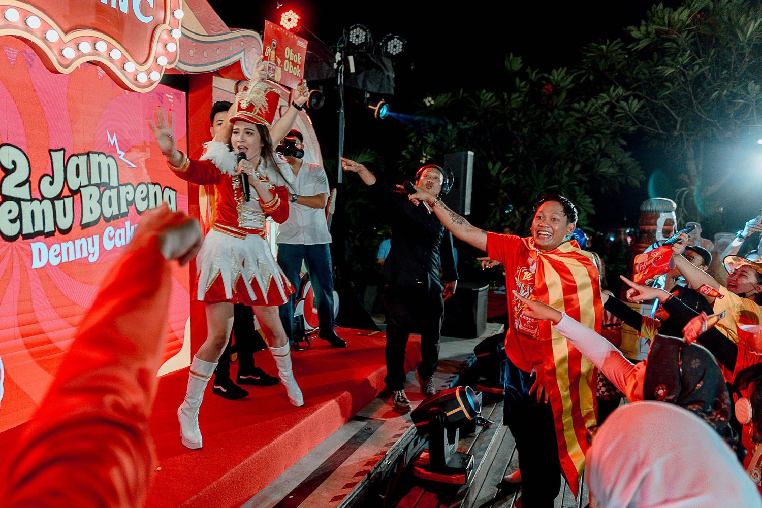 Energetic crowd dancing and jumping at a vibrant red-lit concert or music festival.