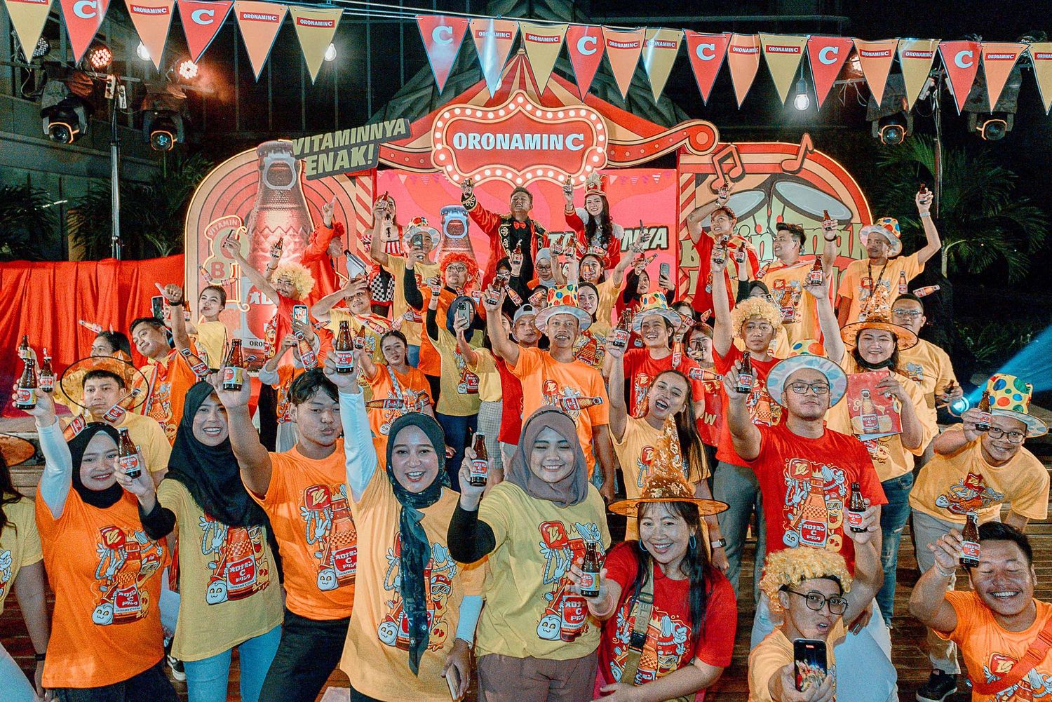 Large group of people wearing colorful t-shirts gather together for a celebratory group photo with festive decorations.