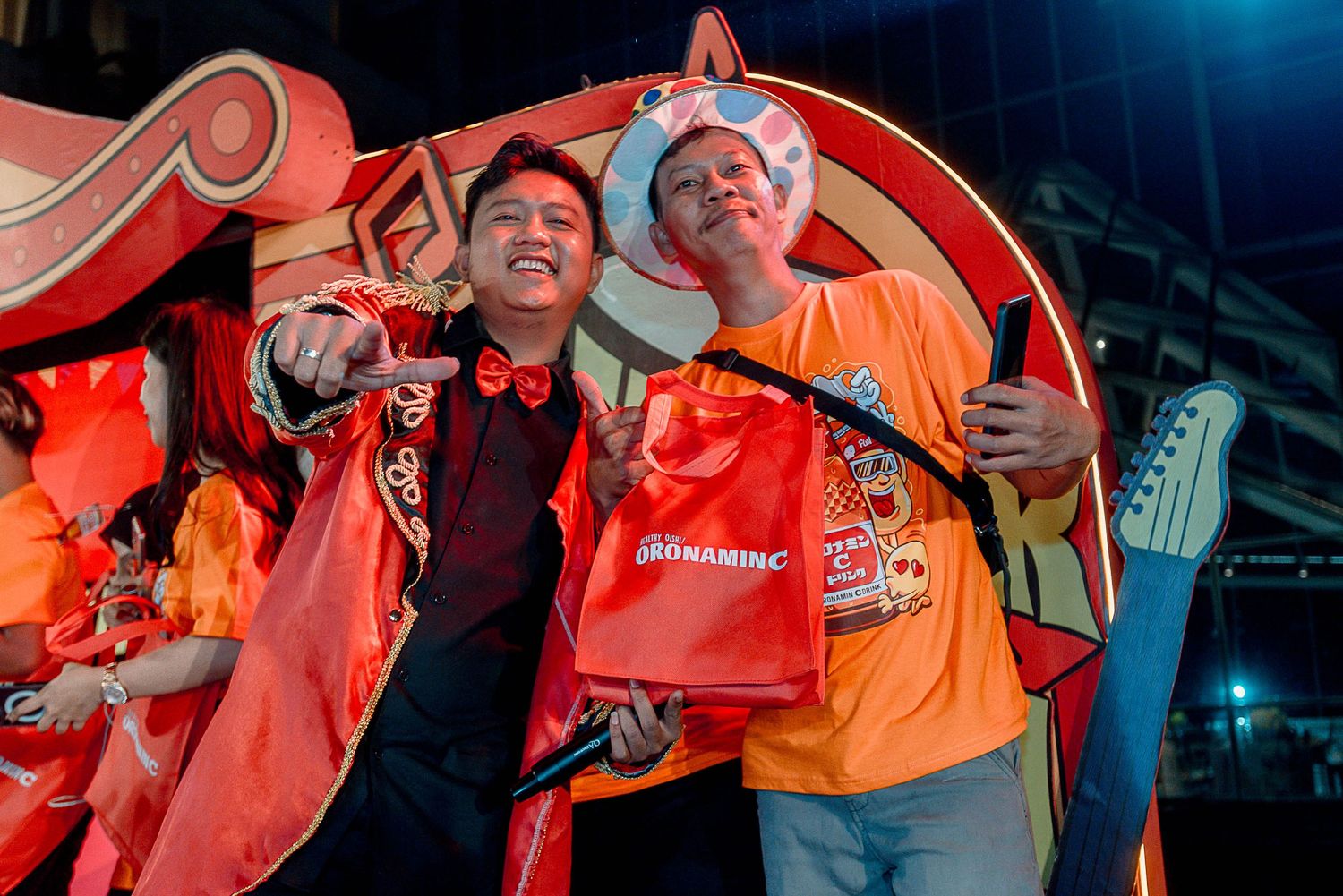 Excited fans in orange and red jerseys celebrate together during a sports event with dramatic lighting.