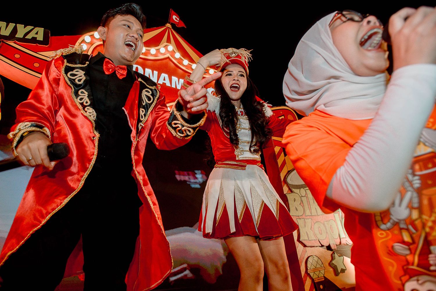 Performers in red and orange costumes dance energetically during a vibrant stage performance.