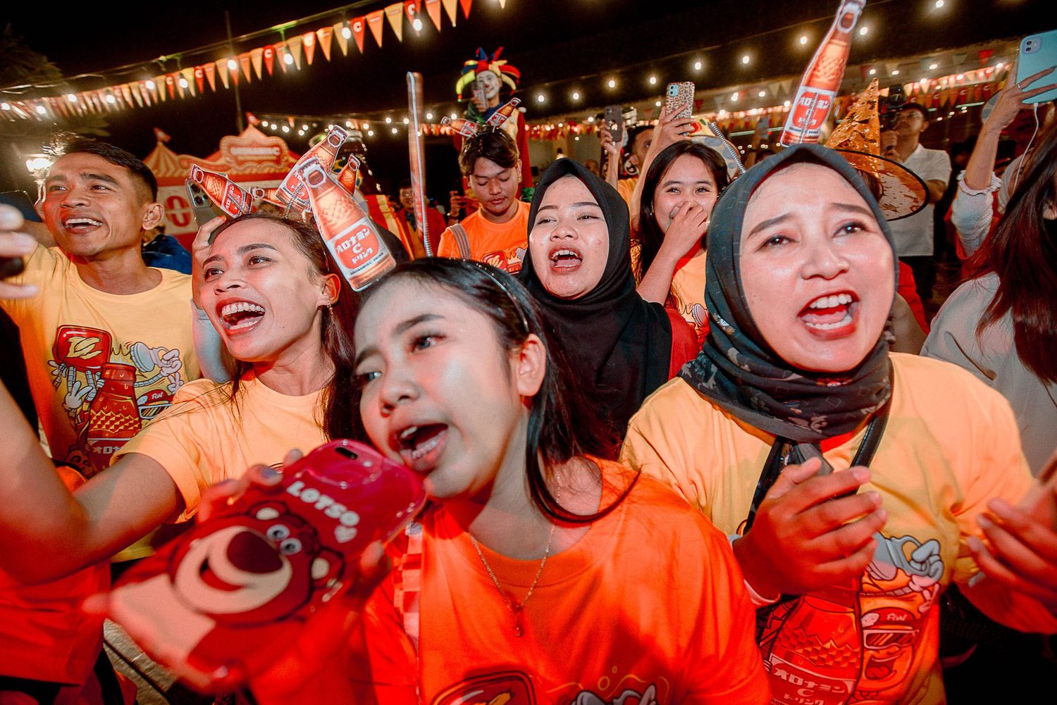 Excited crowd of sports fans cheering in orange team colors at a stadium under glowing lights.