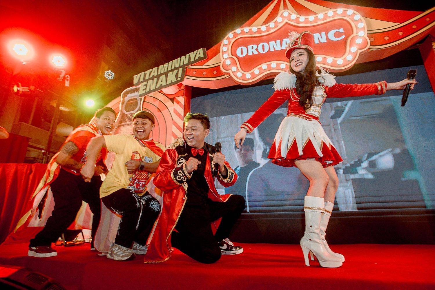 Performers in red and black costumes dancing energetically on stage with illuminated signage in the background.